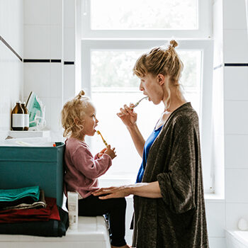 Young Mother With A Child Brushing Teeth In The Morning